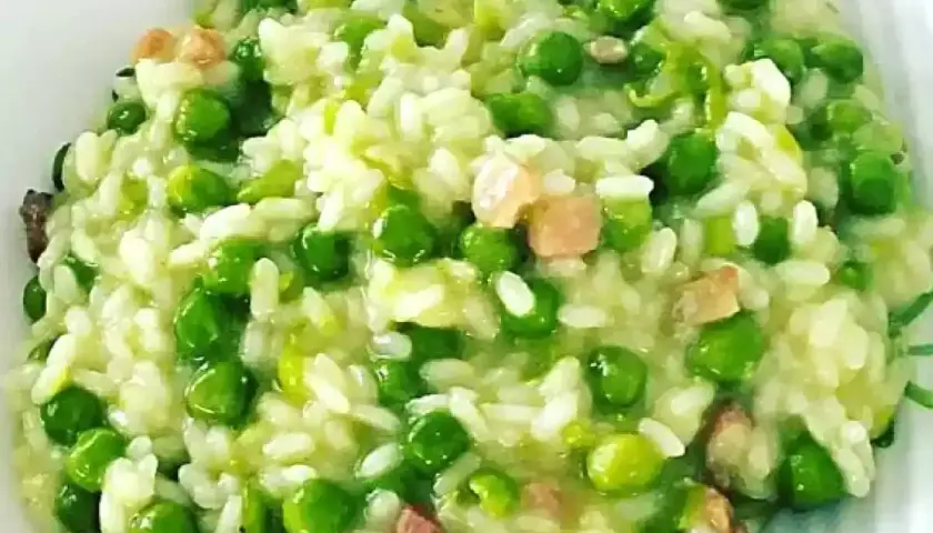 Un cremoso piatto di risi e bisi, con piselli verdi brillanti e cubetti di pancetta croccante, pronto per essere gustato.