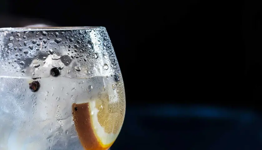 Bicchiere di gin tonic con ghiaccio, bacche di ginepro e fetta d'arancia. La **soda per spritz** rinfrescante crea goccioline sul vetro.