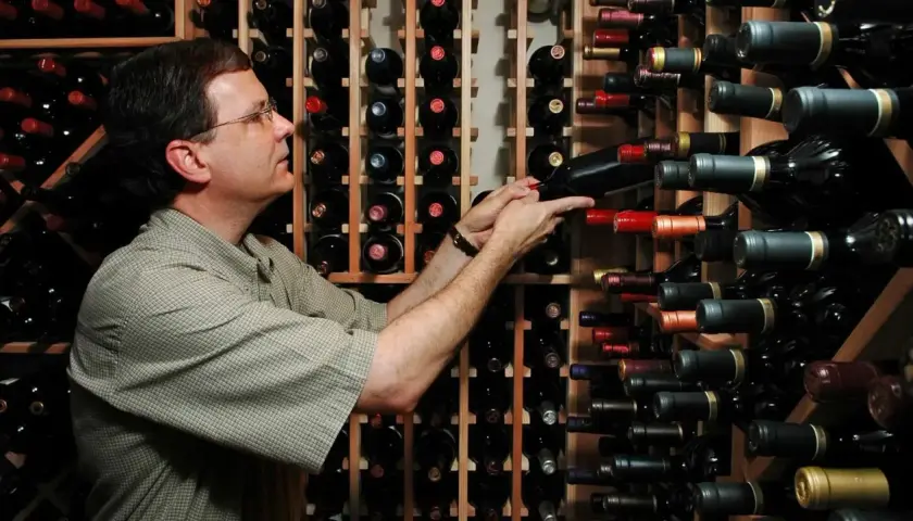 Un uomo sceglie tra una vasta cantina di cru vini, selezionando attentamente una bottiglia.