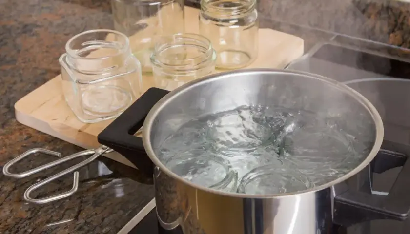 Vapore sale da una pentola piena d'acqua dove si stanno per sterilizzare vasetti pieni. Pinze e altri vasetti vuoti sono sul piano di lavoro.