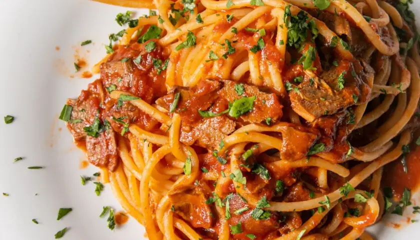 Spaghetti con tonno in scatola, un classico piatto veloce e saporito, condito con sugo di pomodoro e prezzemolo fresco.