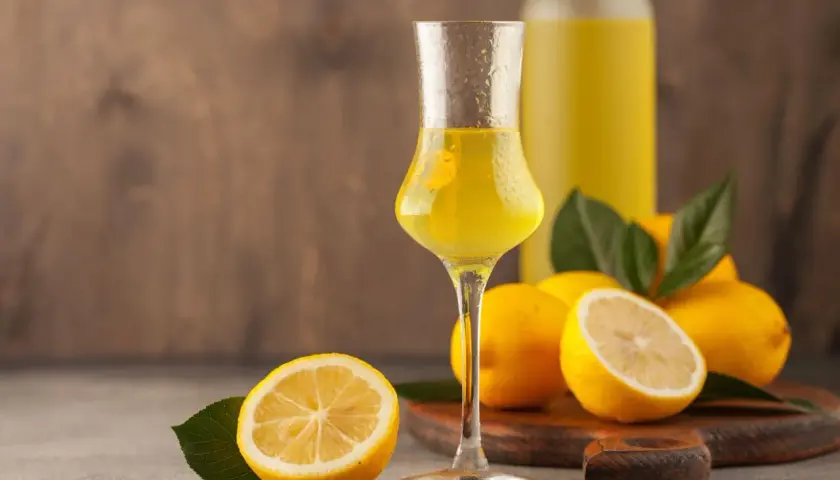 Un bicchiere di limoncello, frutto di un processo di limoncello scientifico, con limoni freschi e una bottiglia sullo sfondo.