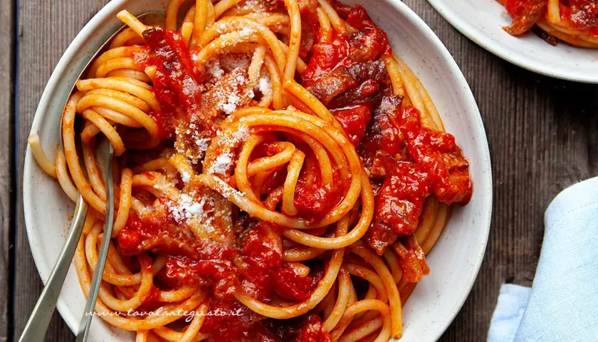 Un piatto invitante di bucatini all'amatriciana ricetta, conditi con sugo rosso e guanciale croccante, spolverati di pecorino.