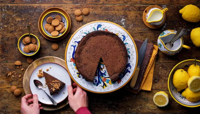 La crescionda spoletina ricetta originale, una torta al cioccolato scuro su un piatto decorato, con amaretti e limoni freschi.