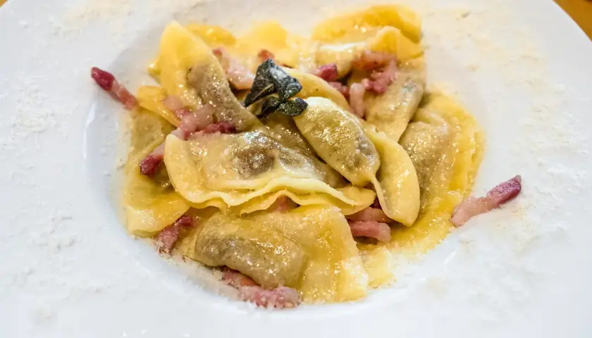 Piatto di casoncelli alla bergamasca con pancetta e salvia, spolverati di formaggio grattugiato.