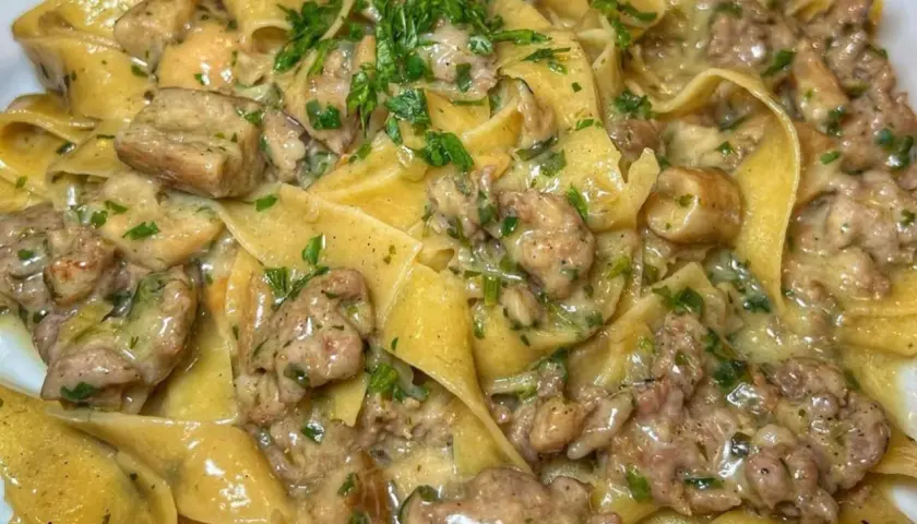 Pappardelle cremose con un saporito sugo di pasta salsiccia e funghi, guarnite con prezzemolo fresco.