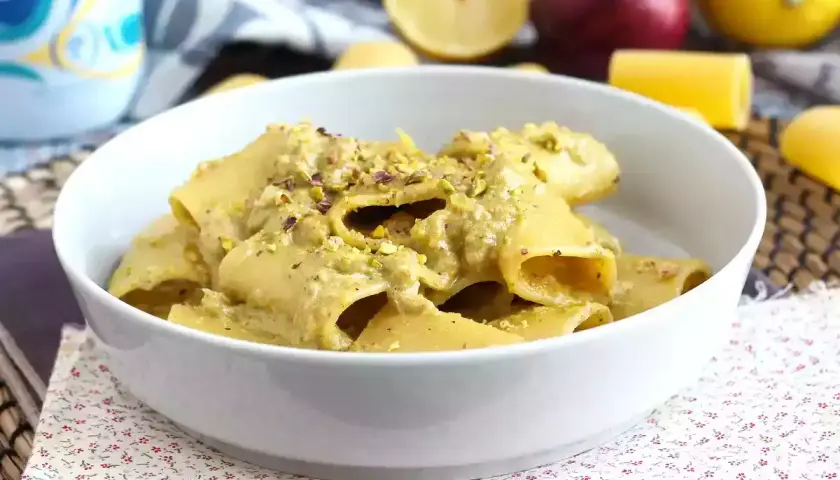 Piatto di pasta tonno e limone, condita con una crema verde e pistacchi tritati, servita in una ciotola bianca.