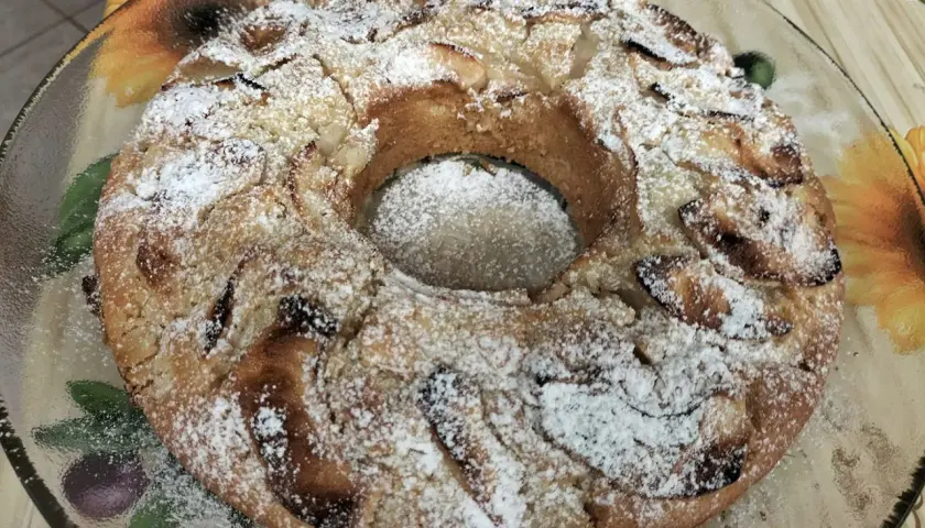 Torta all'acqua soffice e profumata, cosparsa di zucchero a velo, con pezzi di mela visibili.
