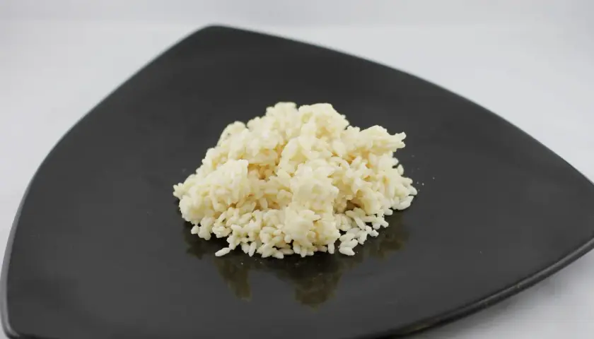 Un mucchietto di riso bianco cotto su un piatto nero, pronto per essere gustato. Ecco come cuocere il riso per un risultato perfetto.