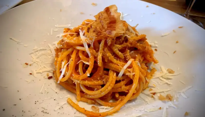 Spaghetti all'amatriciana, un classico piatto romano, perfetto con un vino rosso corposo. Guarnito con guanciale croccante e pecorino.