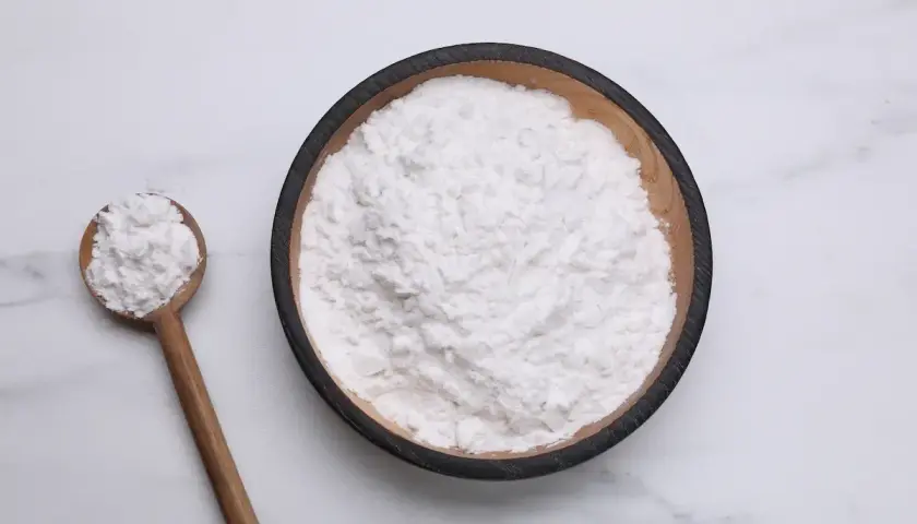 Una ciotola di amido di riso per dolci, con un cucchiaio di legno pieno dello stesso ingrediente soffice.