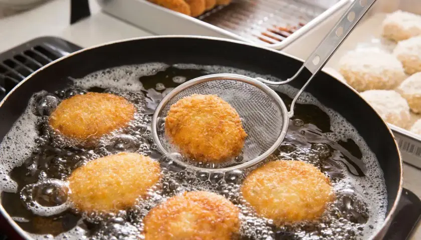 Crocchette dorate che sfrigolano nell'olio bollente, un perfetto esempio di come friggere per ottenere una croccantezza irresistibile.