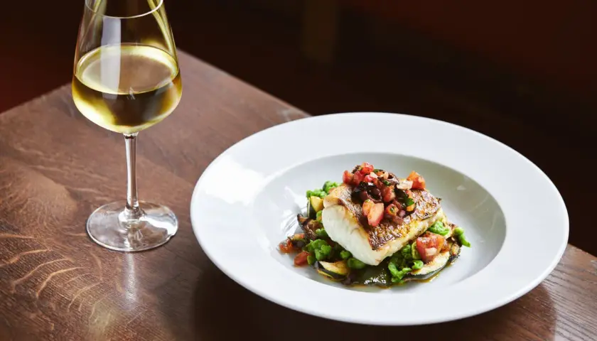 Piatto di pesce con verdure e un bicchiere di vino bianco, perfetti abbinamenti per una ribolla gialla.