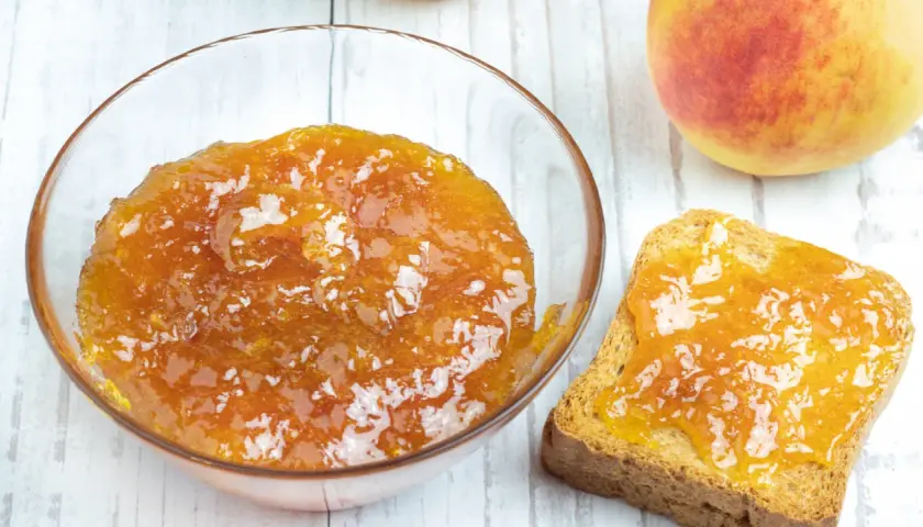 Una ciotola di marmellata di pesche fatta in casa e una fetta biscottata imburrata con la stessa deliziosa marmellata.