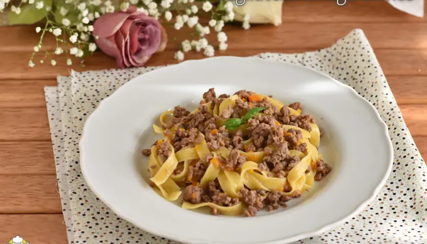 Tagliatelle al ragù bianco, un piatto gustoso con carne macinata e verdure, guarnito con basilico.