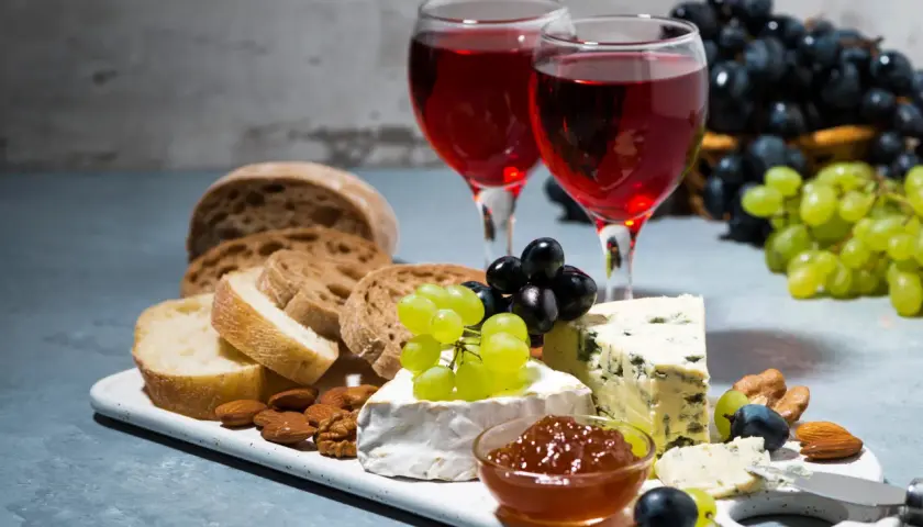 Due calici di rosato vino accompagnano un tagliere con pane, formaggi, uva e frutta secca.