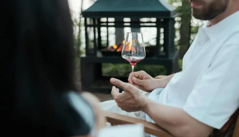 Uomo con barba tiene un calice di vino rosso, mostrando come si tiene il calice di vino per il gambo, vicino a un braciere acceso.