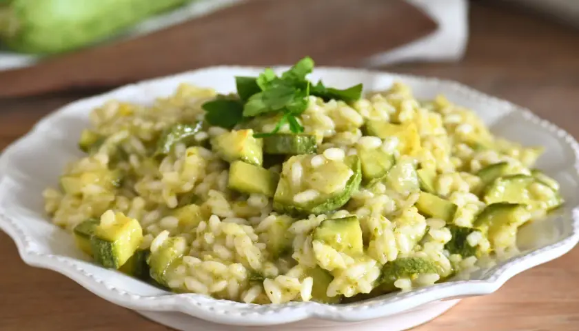 Un cremoso risotto con zucchine, guarnito con prezzemolo fresco, servito in un piatto bianco.