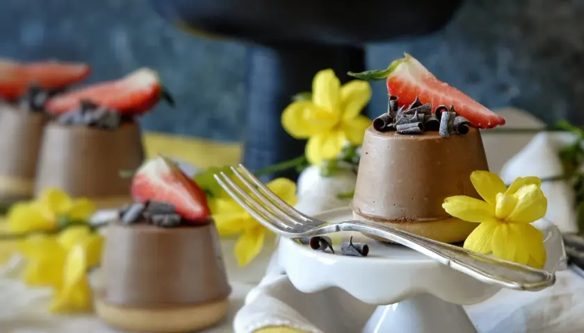 Mini cheesecake al cioccolato con fragola e riccioli di cioccolato, decorati con fiori gialli.