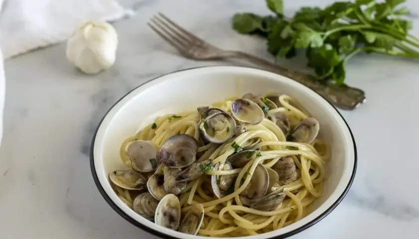 Un piatto invitante di spaghetti alle vongole, con aglio e prezzemolo freschi sullo sfondo.