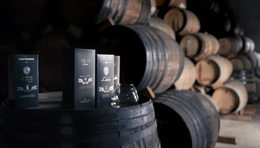 Bottiglie di grappa Castagner su botti di legno. Il significato di grappa barricata è legato all'affinamento in botte, che dona colore e aromi complessi.