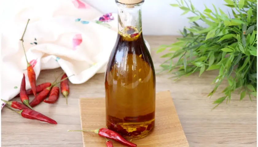 Una bottiglia di olio al peperoncino, con peperoncini rossi secchi sparsi intorno e un tocco di verde sullo sfondo.