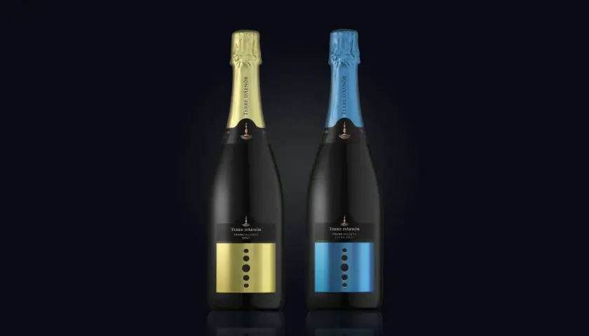 Due bottiglie di Franciacorta Terre d'Aenòr, una con capsula oro e etichetta oro, l'altra con capsula blu e etichetta blu. Entrambe sono Extra Brut, senza zucchero aggiunto.