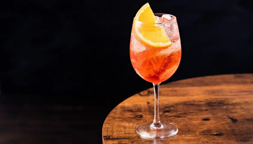 Un bicchiere di spritz Italia, rinfrescante e colorato, con una fetta d'arancia, su un tavolo di legno.