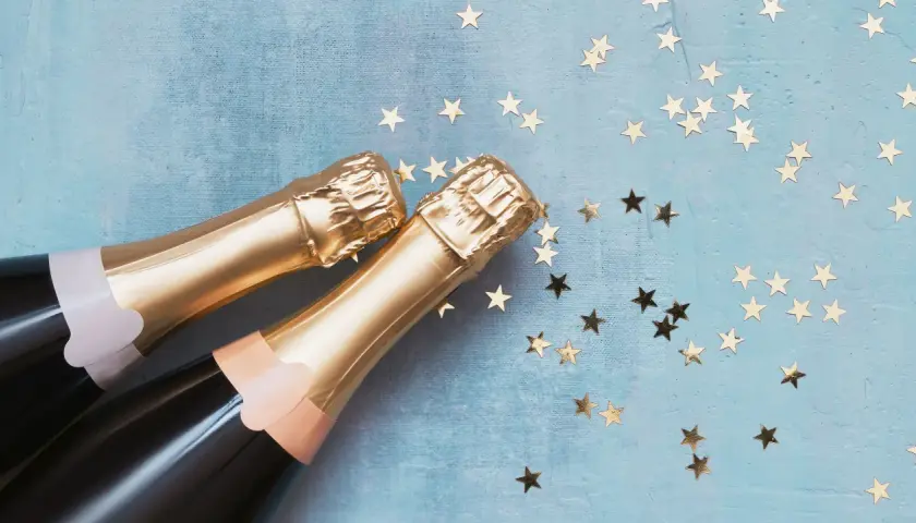 Due bottiglie di spumante dorato su sfondo blu con stelle dorate. Una celebrazione che fa pensare alla differenza tra prosecco e spumante.