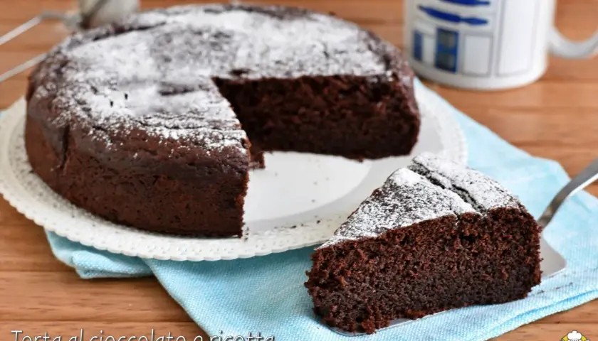 Una deliziosa torta al cioccolato e ricotta, cosparsa di zucchero a velo, con una fetta servita su un tovagliolo azzurro.