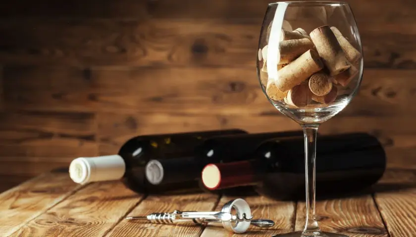 Tappi di sughero in un calice, bottiglie di vino e cavatappi sul tavolo. Un promemoria visivo su come chiudere una bottiglia di vino.