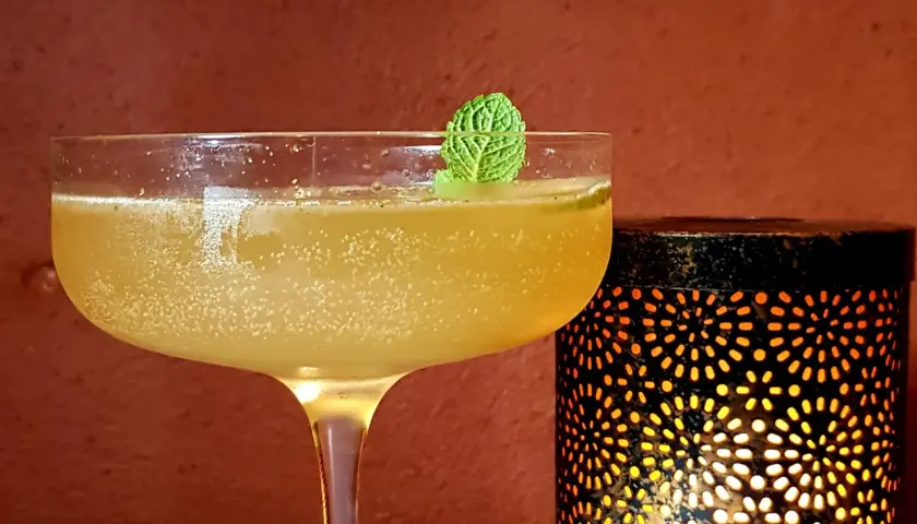 Rinfrescante cocktail con rum e menta, guarnito con una fogliolina verde, accanto a una lanterna decorativa che emana luce calda.