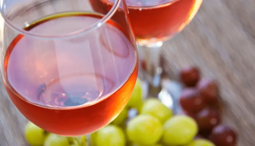 Due calici di vino rosato, frutto della vinificazione in rosato, con grappoli d'uva verde e rossa sullo sfondo.