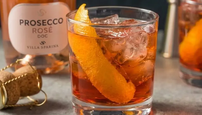 Un Negroni Sbagliato con Prosecco Rosé, guarnito con scorza d'arancia, ghiaccio e una bottiglia di Prosecco Villa Sparina sullo sfondo.