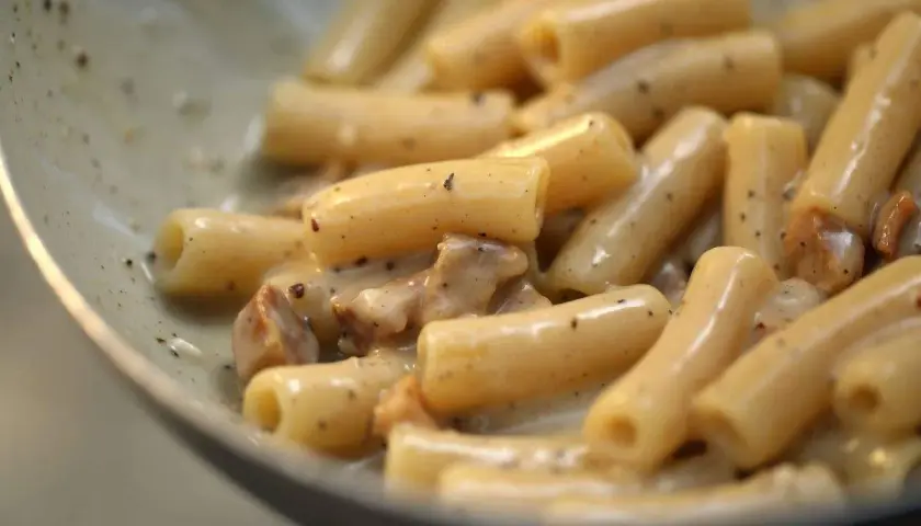 Primo piatto di pasta con guanciale croccante e crema al pecorino romano, un classico saporito.
