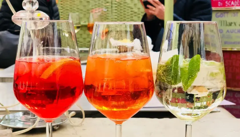Tre spritz colorati, uno rosso con arancia, uno arancione e uno bianco con lime e menta. Perfetti per un aperitivo con il giusto grado alcolico.