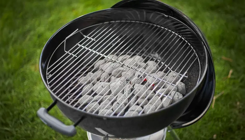 Carbone pronto per accendersi, quanta carbonella per una grigliata perfetta! La griglia è posizionata sopra, in attesa di cibo succulento.