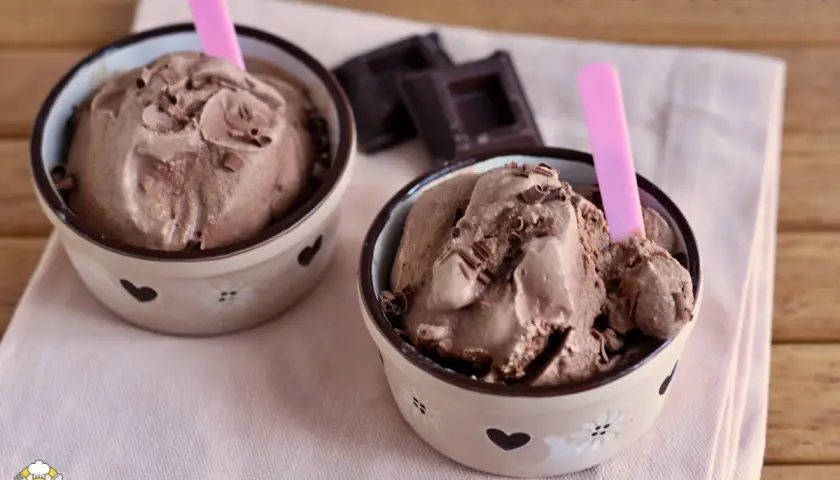 Due coppette di cremoso gelato al cioccolato, guarnite con scaglie di cioccolato e cucchiaini rosa.