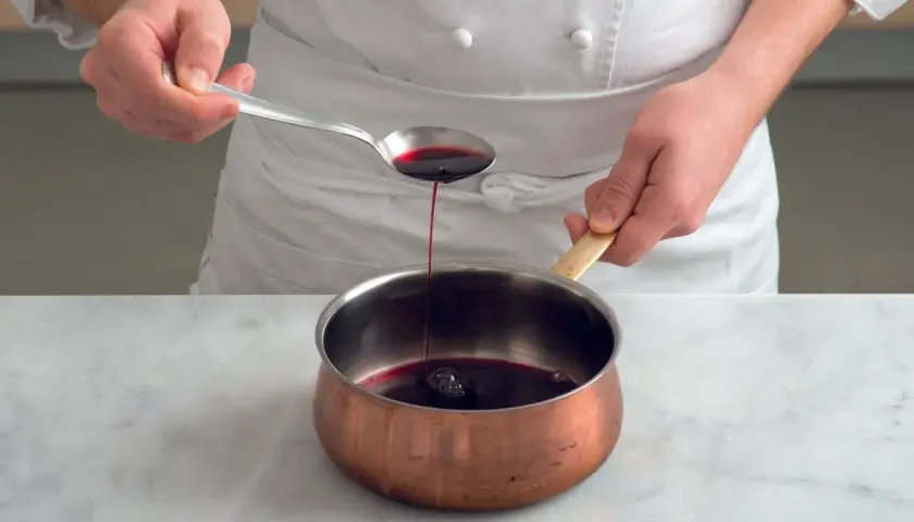 Chef versa un cucchiaio di riduzione di vino rosso in una pentola di rame.
