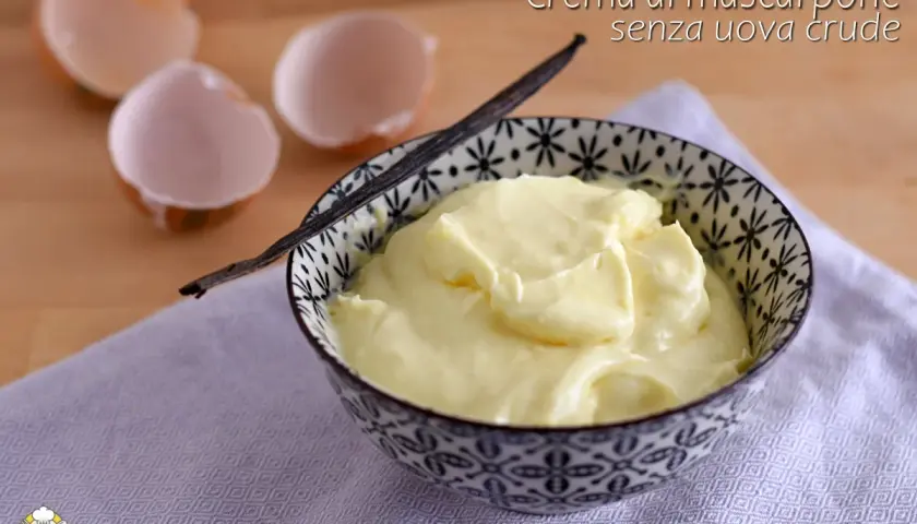 Crema al mascarpone senza uova, soffice e vellutata, servita in una ciotola decorata con un baccello di vaniglia. Guscio d'uovo sullo sfondo.