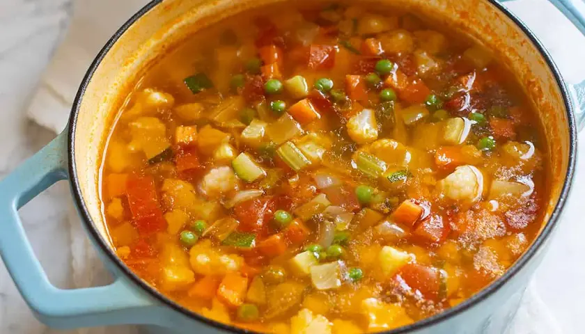 Un fumante minestrone di verdure in una pentola azzurra, ricco di carote, zucchine, piselli e cavolfiore.