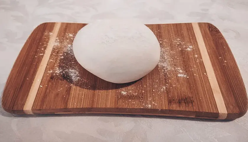 Palla di pasta di zucchero bianca su tagliere di legno, pronta per essere modellata.