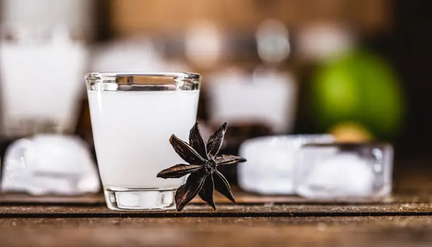 Un bicchierino di cocktail con la sambuca, guarnito con anice stellato, cubetti di ghiaccio e una fetta di lime sullo sfondo.