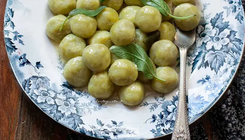 Gnocchi di zucchine soffici e profumati, guarniti con foglie di salvia fresca su un piatto decorato.
