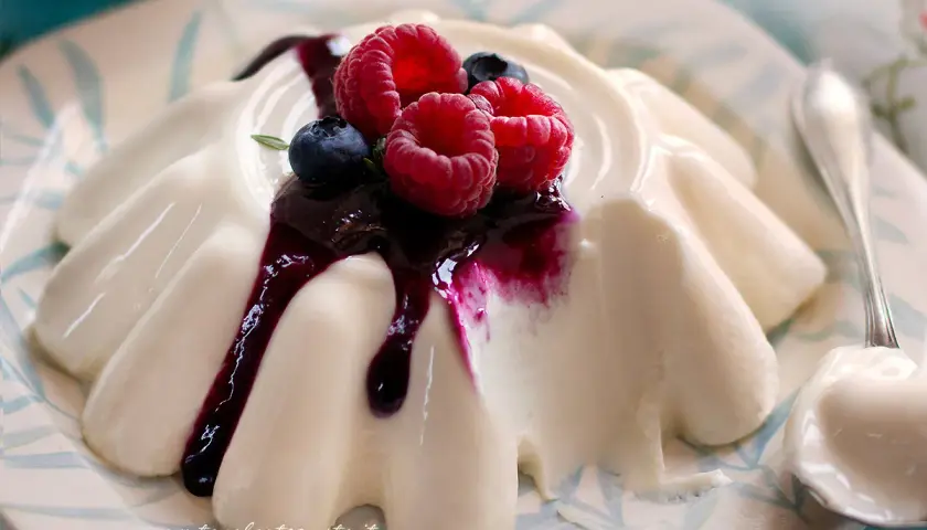 Deliziosa panna cotta con frutti di bosco e salsa ai mirtilli, servita su un piatto decorato.