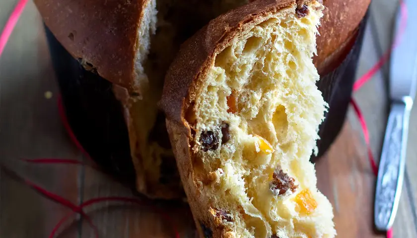 Un dolce panettone casalingo, soffice e profumato, con canditi e uvetta. Una fetta mostra la sua morbidezza e il colore dorato.