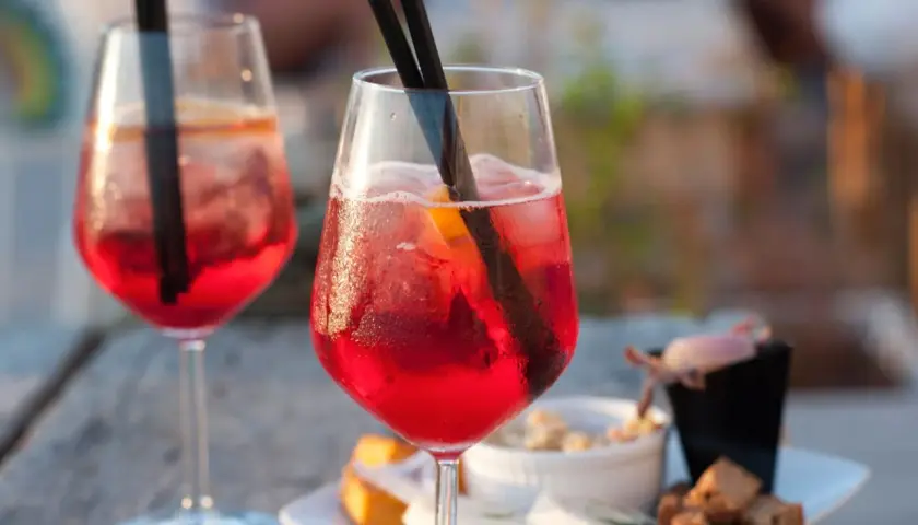 Due cocktail rossi con ghiaccio e arancia, accompagnati da stuzzichini. Perfetti per un aperitivo, ecco la pirlo bianco ricetta.