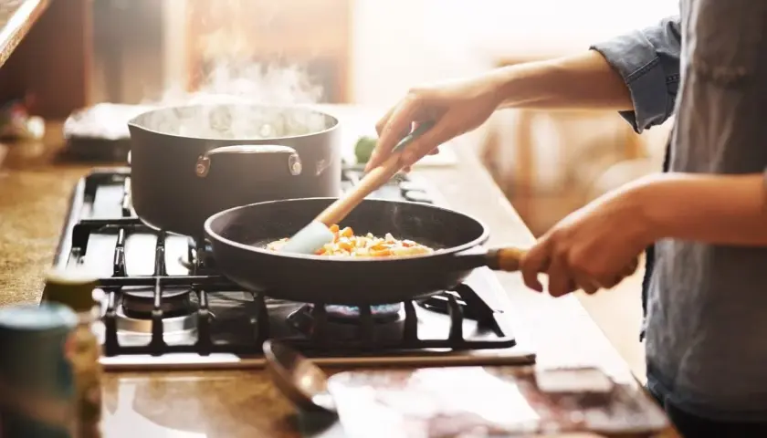 Mani che mescolano verdure in padella, mentre l'acqua bolle in pentola. Un'immagine che evoca il **macerare significato** in cucina: preparare ingredienti con cura.