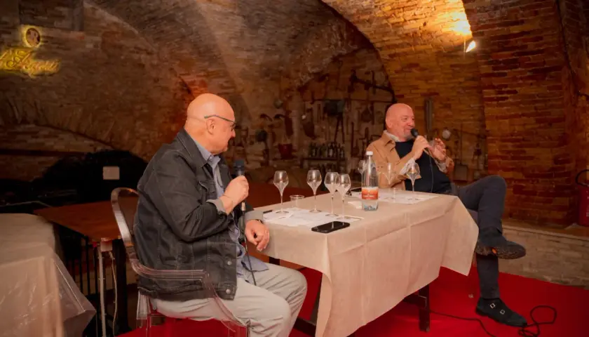 Due uomini discutono del metodo champagne in una cantina storica, con bicchieri da degustazione pronti.