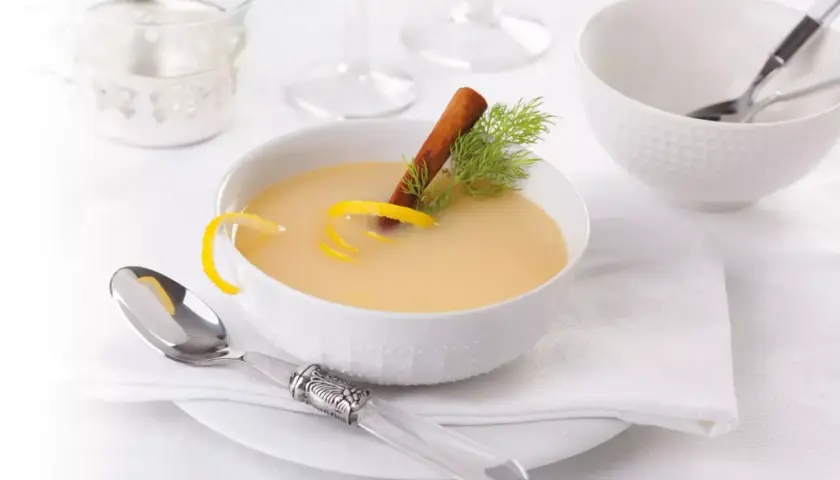 Una ciotola di cremosa salsa al vino bianco, guarnita con scorza di limone, cannella e aneto. Servita con un cucchiaio d'argento.